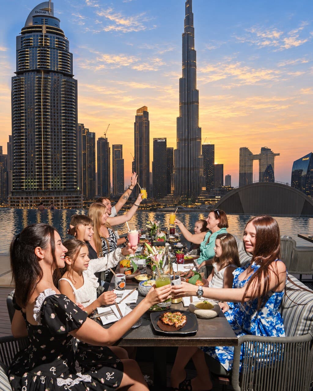 Families raising their glasses at Flamingo Brunch on the NAZCAA terrace, the Burj Khalifa behind them at sunset