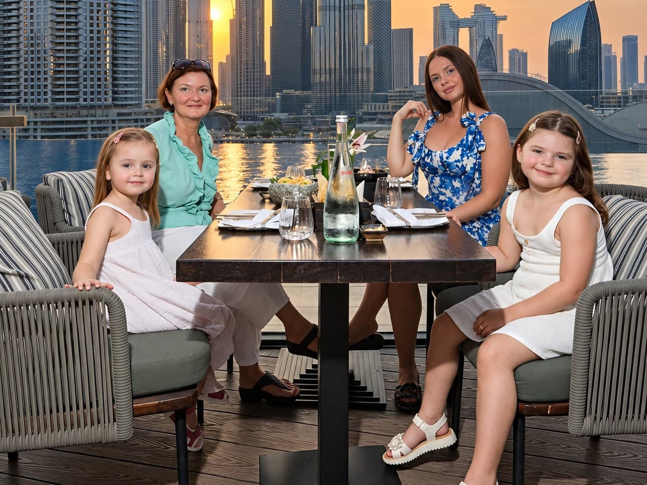Two mothers and their daughters at a terrace table at NAZCAA, the Burj Khalifa behind them at sunset